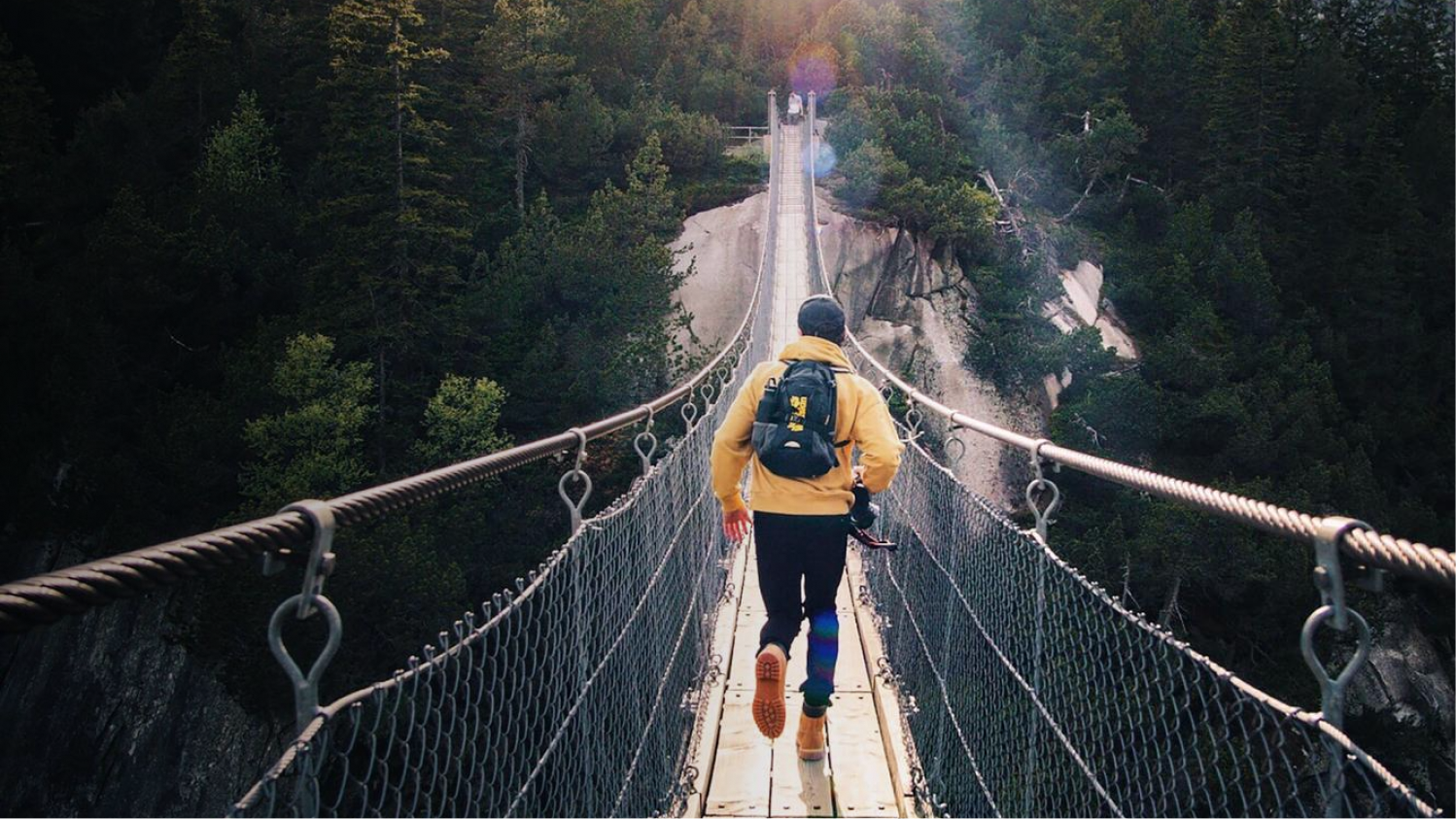 Mann läuft in atemberaubender Landschaftskulisse über eine Hängebrücke