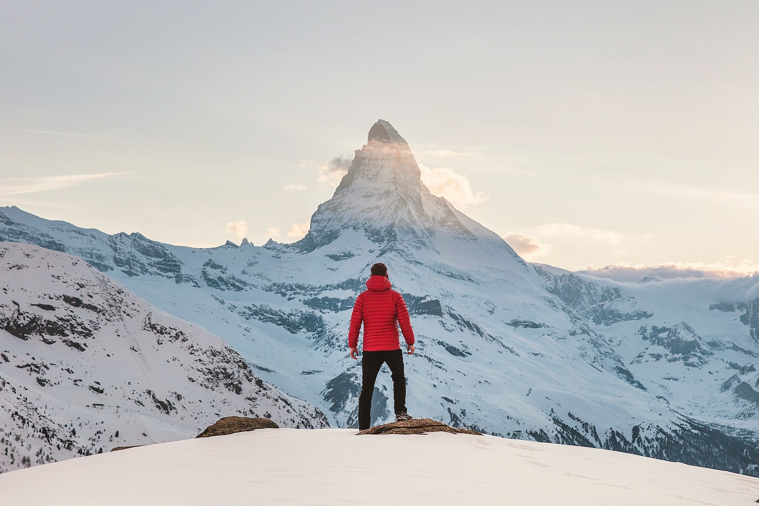 Person in roter Winterjacke, die tagsüber auf einem verschneiten Berg steht