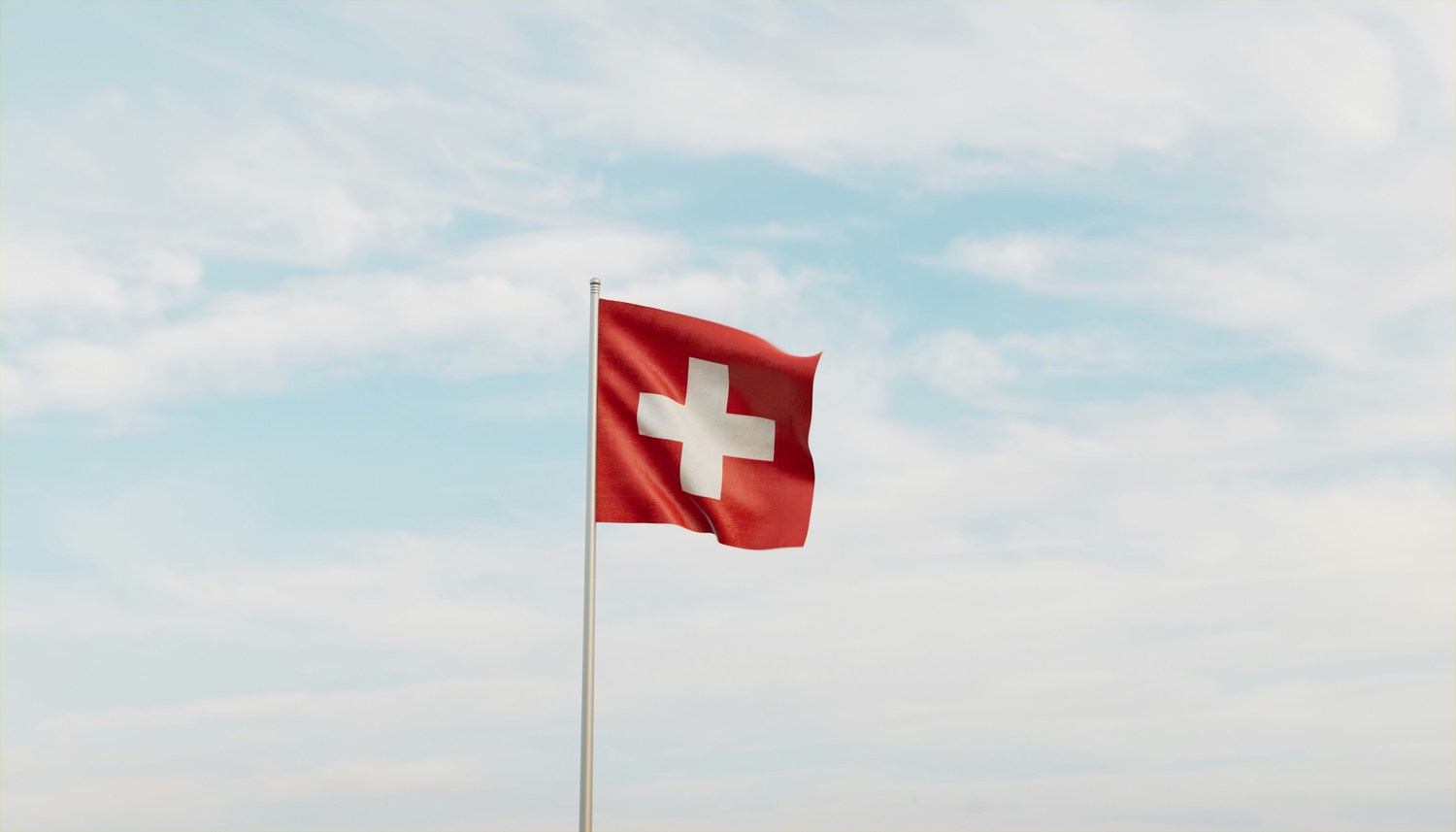 Schweizer Flagge weht an einem Fahnenmast vor einem bewölktem Himmel.