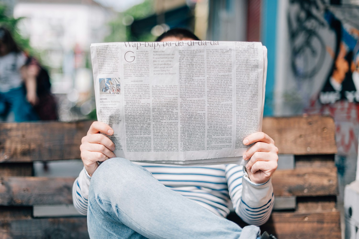 Ein Mann sitzt auf einer Bank und liest eine Zeitung.